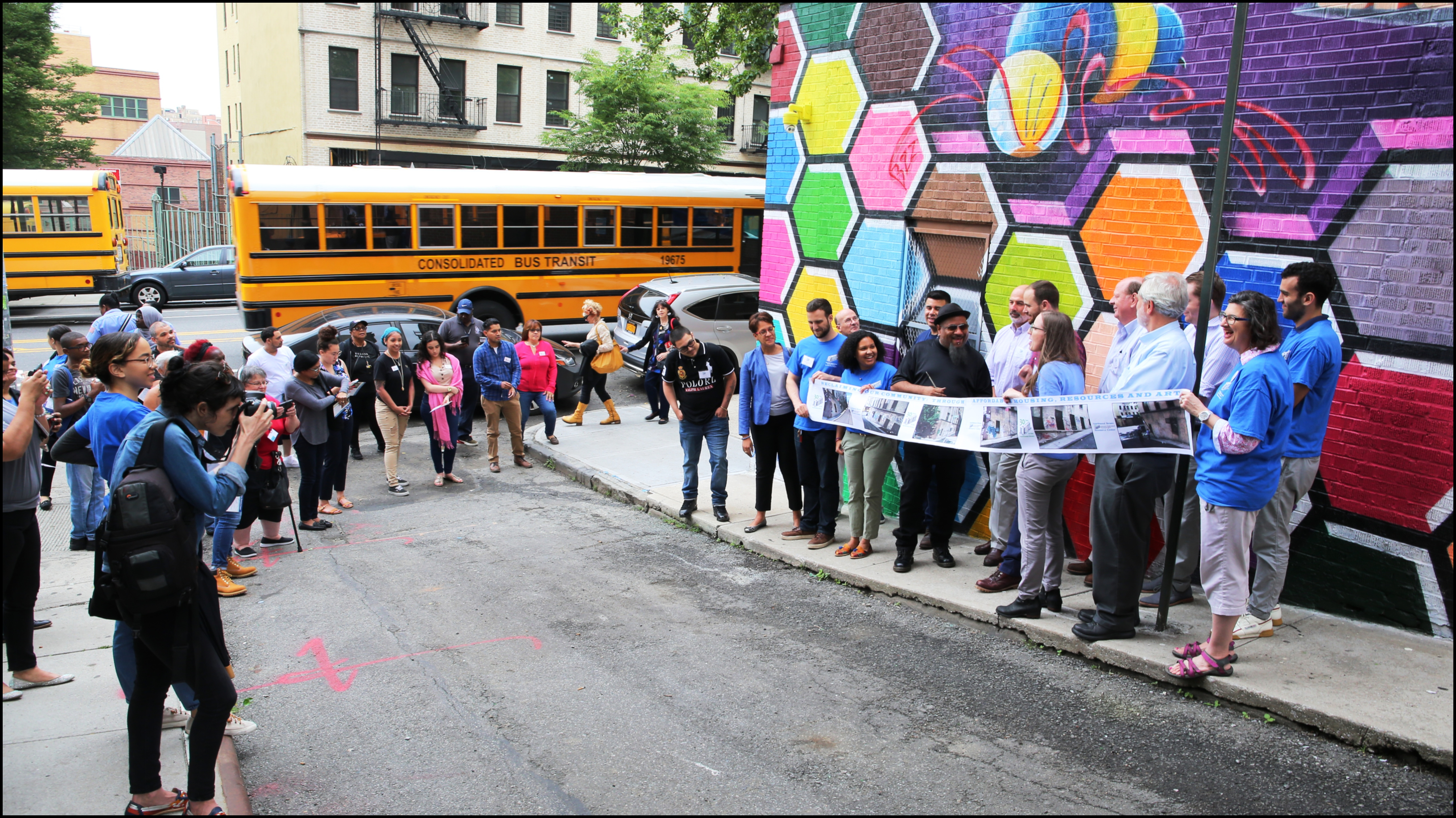 The view down Kingsland Plaza onto West Tremont Avenue never looked so good! The crowd of tenants, KingBee fans, passersby, and partners look on as KingBee gets ready to unveil his bee-utiful mural on the site of one of UNHP’s affordable housing buildings.